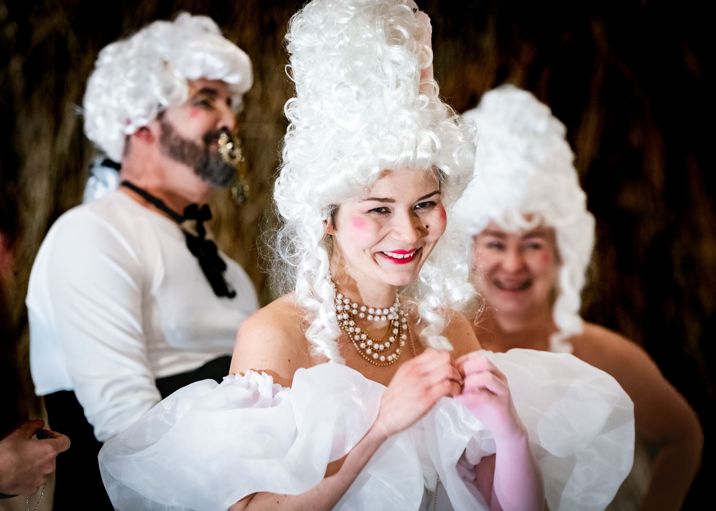 Kobieta w białej peruce i koralach z uśmiechem, w otoczeniu innych osób w rokokowych strojach i makijażu. - Brzeg, Lubin, Oława, Legnica, Wrocław, Opole - zoptymalizowana wersja do szybkiego ładowania