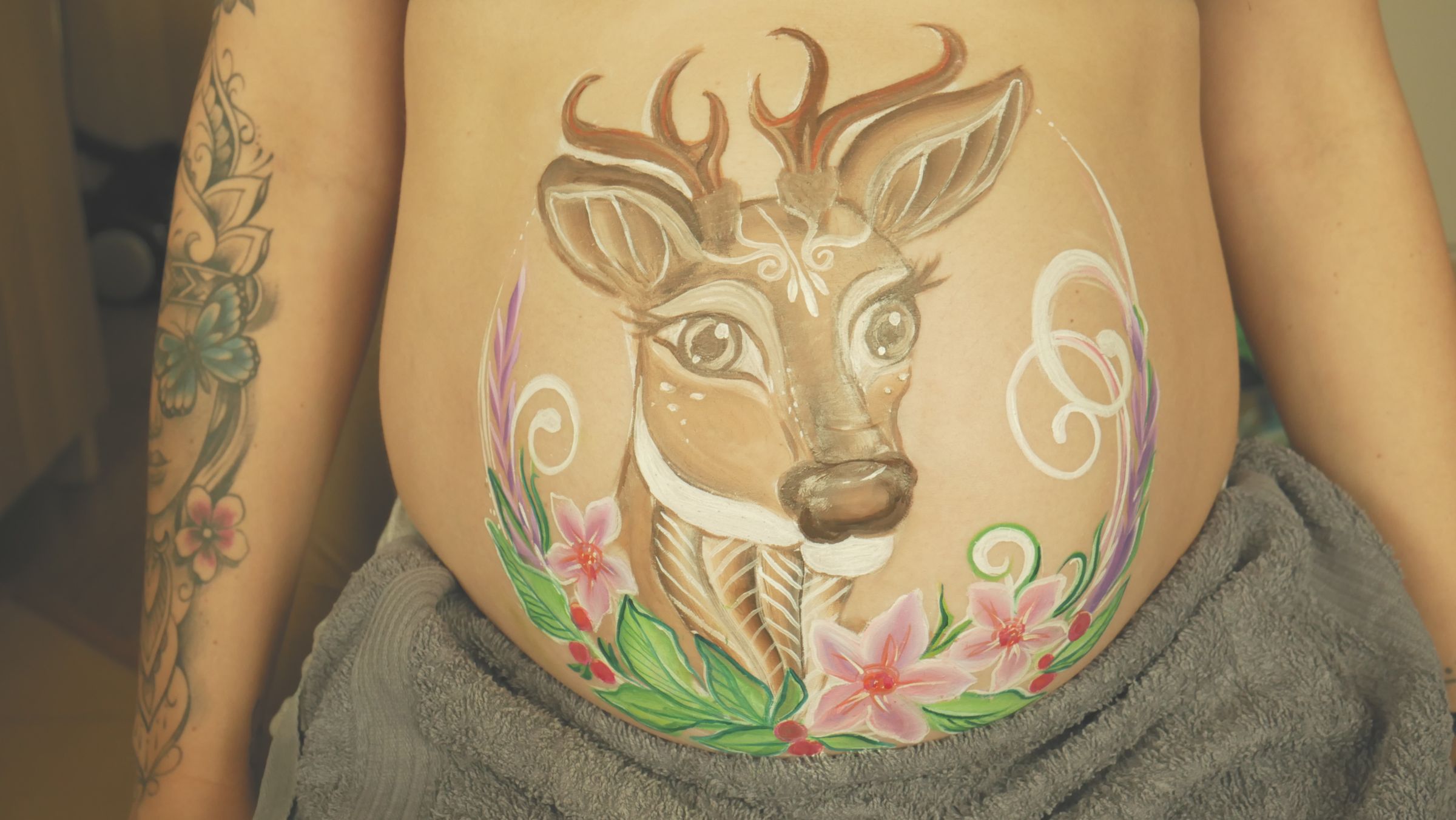 Pomalowany ciążowy brzuszek z wizerunkiem jelonka otoczonego kwiatami – symbol łagodności i nowego życia. Delikatny belly painting w pastelowych barwach, inspirowany naturą i macierzyństwem. - Brzeg, Lubin, Oława, Legnica, Wrocław, Opole - zoptymalizowana wersja do szybkiego ładowania
