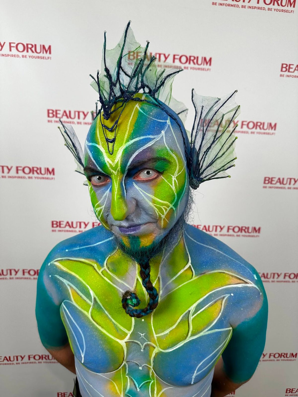 Zbliżenie Leśnego Strażnika: zielono-niebieska twarz, białe linie i ażurowe ozdoby głowy podczas Beauty Forum.