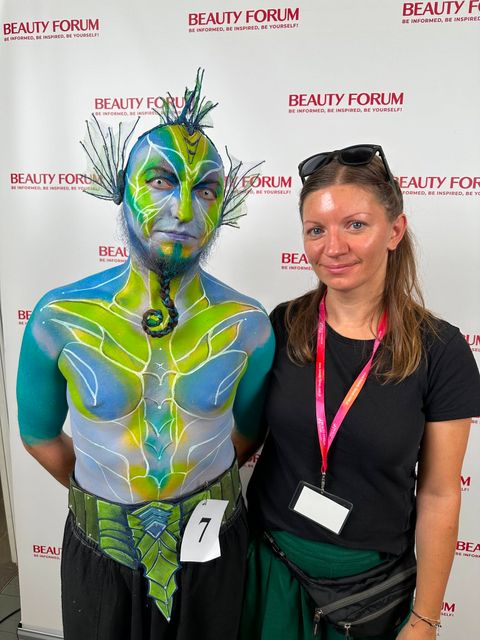 Model w zielono-niebieskim body paintingu Leśnego Strażnika obok kobiety na tle ścianki Beauty Forum.