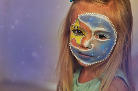 Painted face of a girl with a moon and star motifdecorated with pearls and resembling a starry sky - full resolution